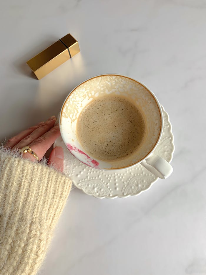 embark A cozy scene with a ceramic cup of coffee on a white table, sweater, and lipstick mark.